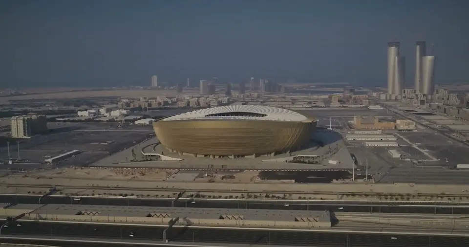 Aerial view of Lusail Stadium, Qatar, in daylight haze: a gold bowl in flat land, with towers on the horizon.