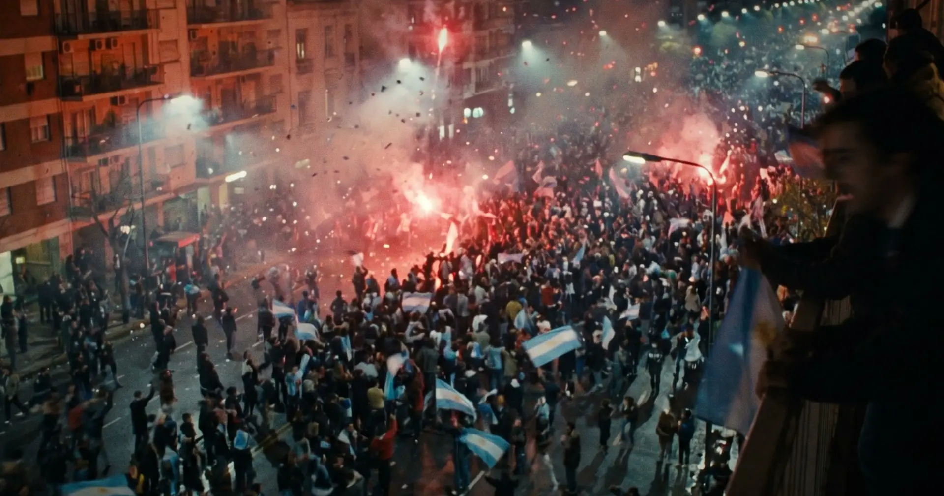A huge street crowd from above at night, red flares and smoke between apartment blocks.