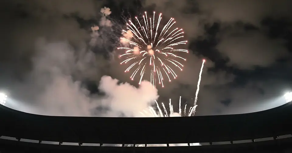 Fireworks and white smoke above the dark rim of a stadium.
